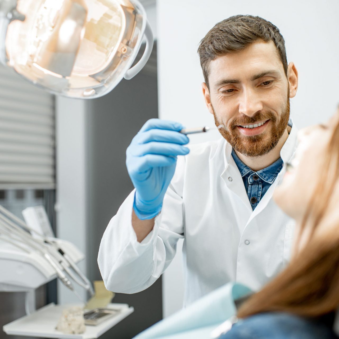 Handsome dentist making dental examination to a young woman patient in the dental office